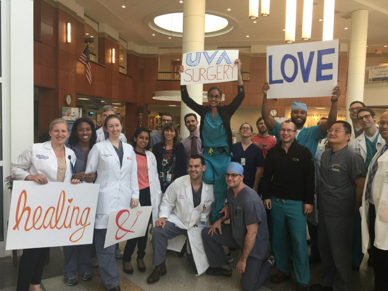 Surgery residents standing in the hospital lobby holding signs that say "Healing and Love" and "UVA Surgery"